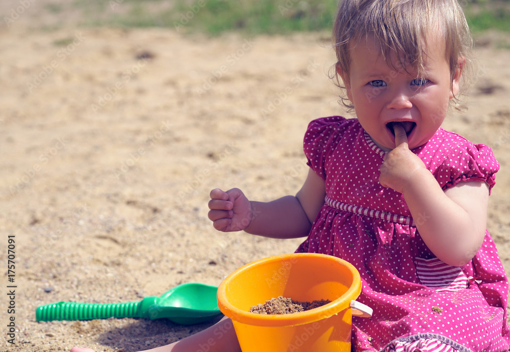 Little girl plays with toys in the sand. The girl stuck her finger with the sand in her mouth. The concept of education and child development. Little girl plays with toys in the sand. The girl stuck her finger with the sand in her mouth. The concept of education and child development.