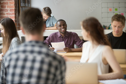 Young smiling african american entrepreneur talking to female coworker. Multiethnic team of colleagues communicate during workflow  employee inquiring about work strategy  specifics in business plan.