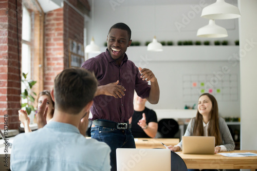 African american office worker dancing surrounded by colleagues. Happy entrepreneur performing victory dance, celebrating great achievement at work. Team of coworkers cheering him by clapping hands.
