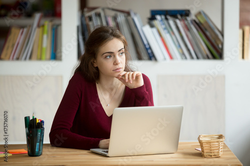 Thoughtful young female entrepreneur in front of laptop. Casual businesswoman thinking about possibility of seeking new business opportunities. Freelance small business owner daydreaming about future.
