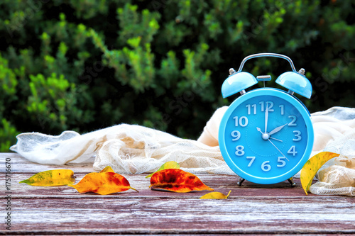 Image of autumn Time Change. Fall back concept. Dry leaves and vintage alarm Clock on wooden table photo