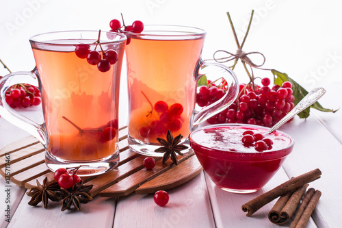 Vitamin healthy viburnum berry warm drink in glass cups with fresh raw viburnum berries and cinnamon sticks, anise stars on a white kitchen table. 