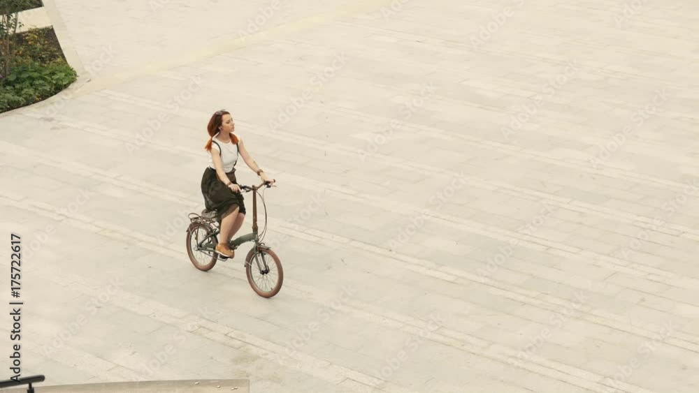 Woman cyclist riding a bike on paved road at square on summer day