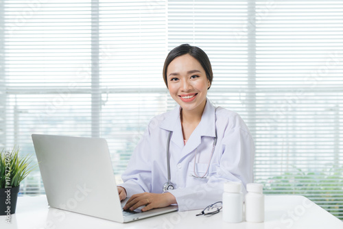 Female doctor working with laptop at office desk and smiling