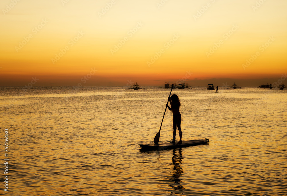 Silhouette of a girl floating on on the sup surfboard at sunset over the sea at Boracay island Philippines