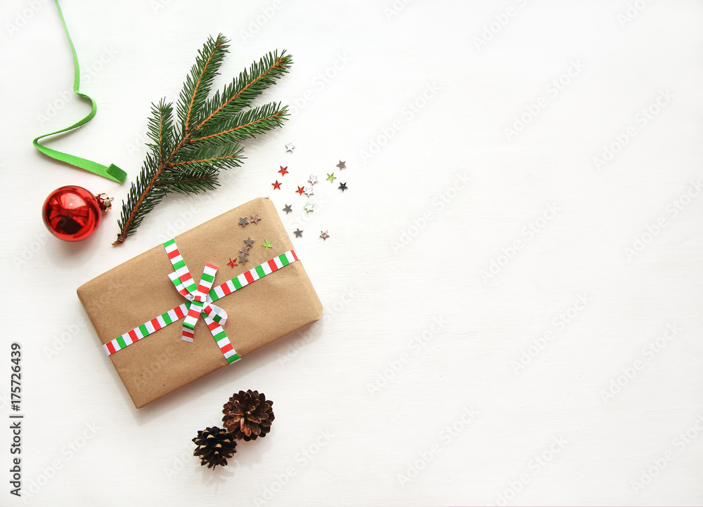 Obraz premium Christmas or New Year background with copy space. Christmas composition made of decorations: gift, red ball, fir branch, pine cones, fir branch and gift on textured white background. Flat lay.