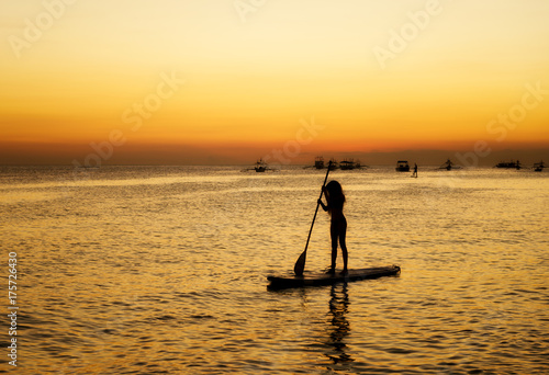 Silhouette of a girl floating on on the sup surfboard at sunset over the sea at Boracay island Philippines © len4foto
