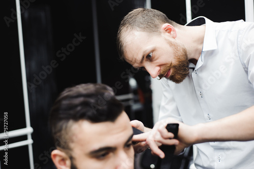 Master cuts hair and beard of men in the barbershop, hairdresser makes hairstyle for a young man