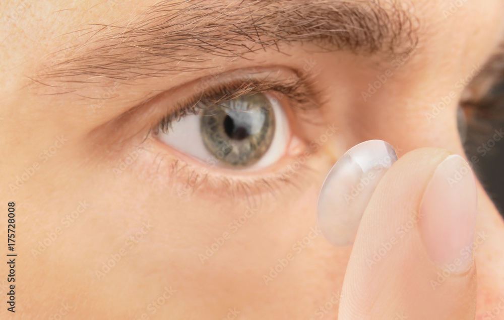 Obraz premium Young man putting contact lens in his eye, closeup