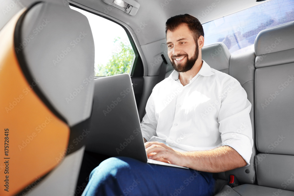Handsome man with laptop on backseat of car