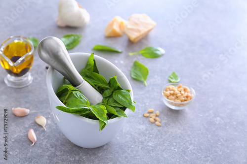 Mortar with pestle and basil leaves on table