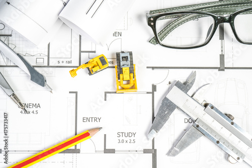Top view of architect drawing on non identified architectural project with various of tools such as divider pencil eye glassed and small heavy equipment machine toys.