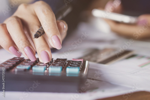 business woman hand counting monthly expenses on calculator with blur background of credit card on table and another hand holding smart phone