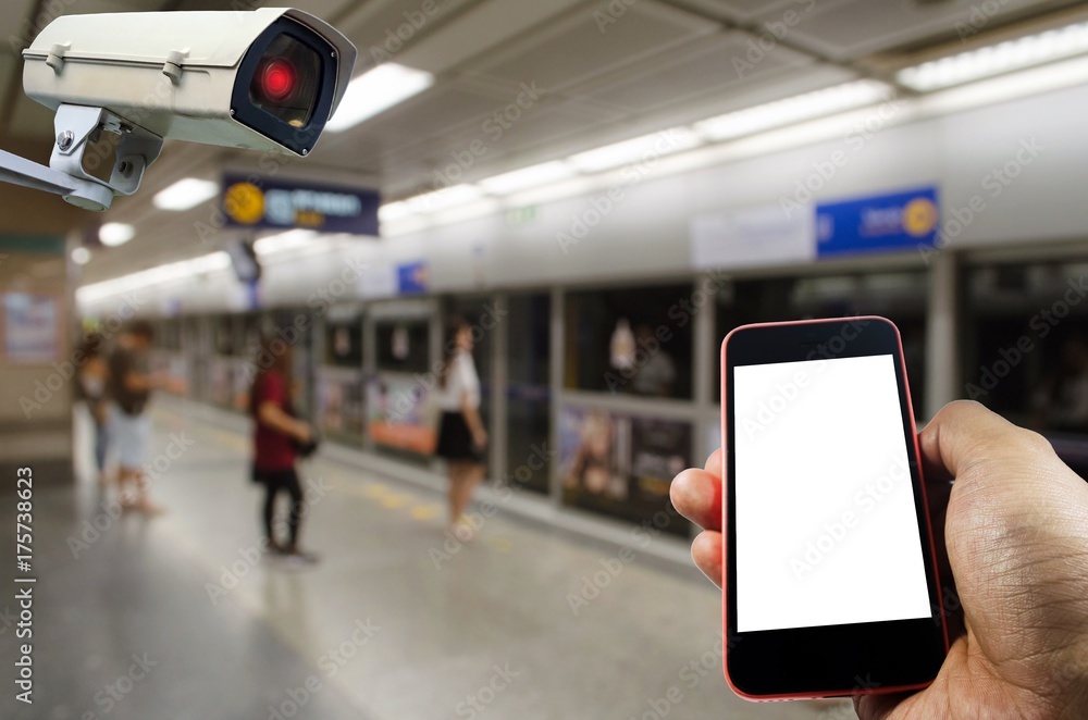 hand holding smart phone monitoring and CCTV security indoor camera system operating with people waiting for subway at train station, internet, surveillance security, safety technology concept hand holding smart phone monitoring and CCTV security indoor camera system operating with people waiting for subway at train station, internet, surveillance security, safety technology concept