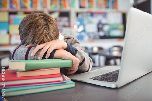 Tired schoolboy resting on stack of in classroom