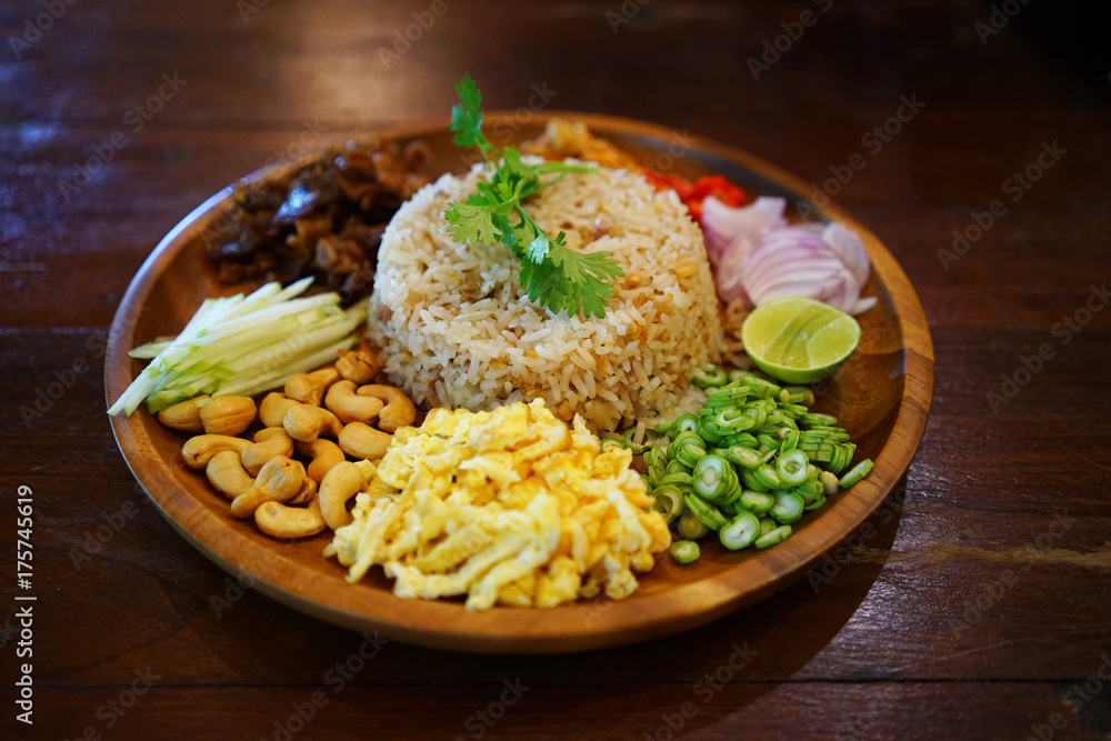 Kao Cluk Ka Pi or Mixed Cooked Rice with Shrimp Paste on the wooden round dish. Thai Traditional food. Selective focused. - obrazy, fototapety, plakaty 