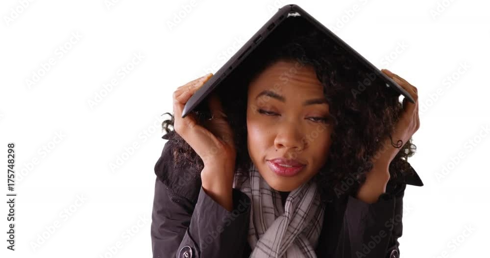 Worried black female using laptop to shield herself from rain in studio Worried black female using laptop to shield herself from rain in studio