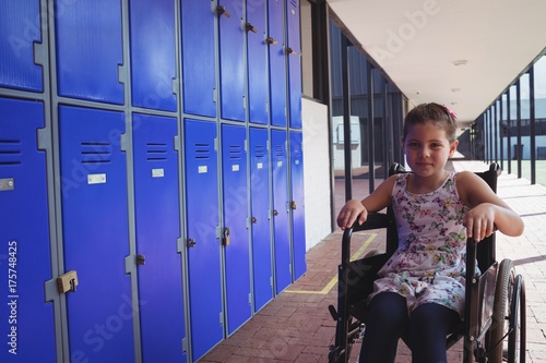 Portrait of schoolgirl sitting on wheelchair by lockers photo