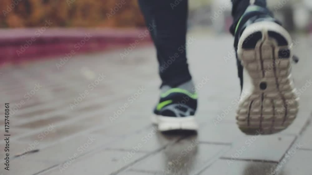 Man running on a wet concrete road. Close up tracking shot of legs of unidentified person jogging. Sport, healthy lifestyle concept. Man running on a wet concrete road. Close up tracking shot of legs of unidentified person jogging. Sport, healthy lifestyle concept.