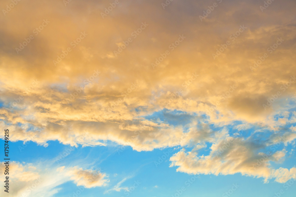 Golden fluffy clouds illuminated by the sunset against a blue sky (background)