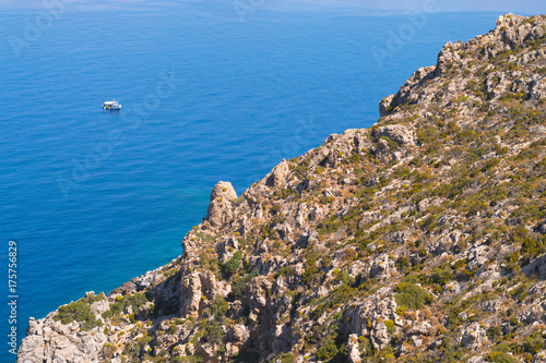 Landscape blue ocean and small boat from rocky trekking/hiking path on Greek island Telendos. Popular hiking destination on island Kalymnos, pure nature.