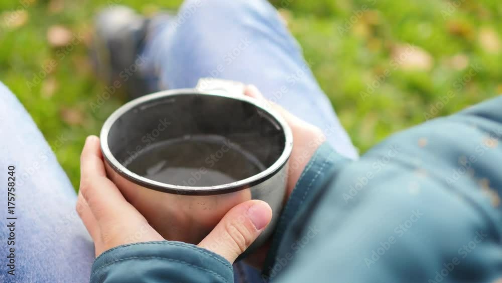 In autumn Park guy sitting on the lawn and drink hot tea, walk in the fresh air. Close-up of hands In autumn Park guy sitting on the lawn and drink hot tea, walk in the fresh air. Close-up of hands