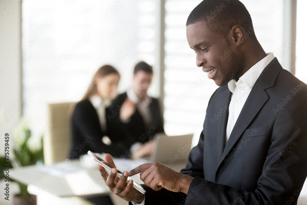 Φωτογραφία African american businessman using mobile phone in office caucasian woman and man in formal wear sitting at desk in background