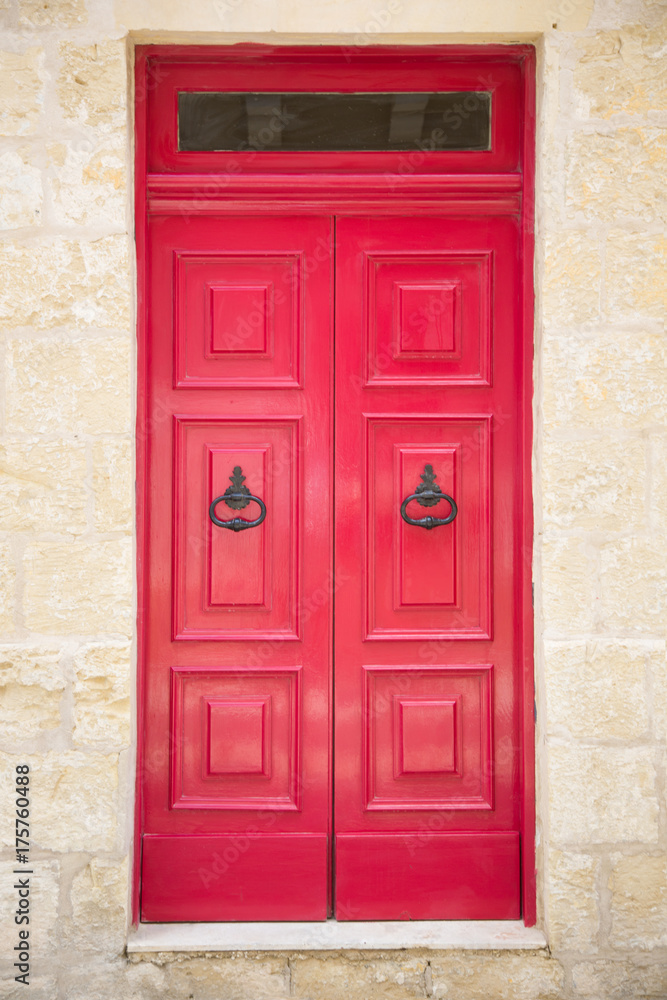 Red painted old wooden door with black iron handle in medieval city street