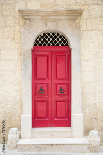Red painted old wooden door with black iron handle in medieval city street