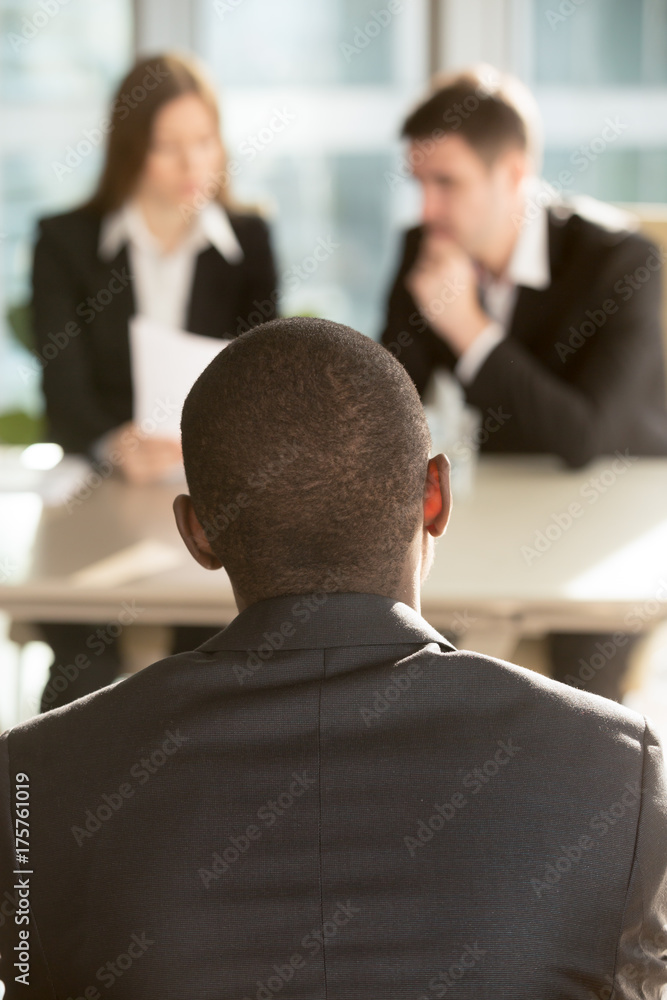 African american male job candidate waiting for hiring decision on job interview, caucasian employers reading resume on background. Millennial black man interested in vacancy searching his first job African american male job candidate waiting for hiring decision on job interview, caucasian employers reading resume on background. Millennial black man interested in vacancy searching his first job