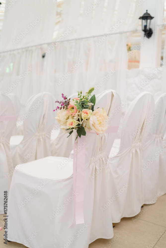 Beautiful flower arrangement on white wedding chairs on each side of archway, selective focus. Empty chairs with white cloth for guests on wedding ceremony, free space