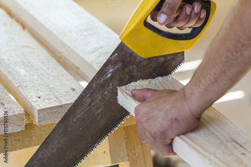 Fotografie Carpenter hand with saw cutting wooden boards