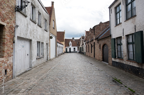 Fototapeta Naklejka Na Ścianę i Meble -  Quaint little cobblestone street lined with small traditional brick houses in Bruges Belgium. Vernacular housing and cobbled road in Belgium. Quaint European street, no people.