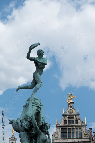 Copper statue of Brabo in the Grote Markt in Antwerp  Belgium on a sunny afternoon with blue skies and puffy clouds. Antwerp City Hall in the background.