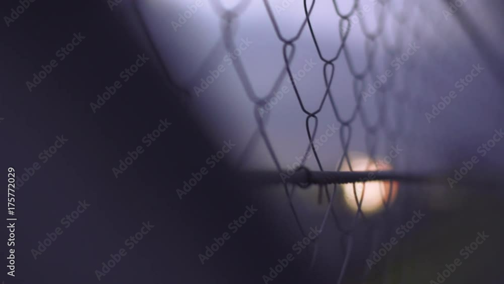 Wire fence. Closeup and rack focus of steel net. Security protection barrier at the racing track in the dusk. Industrial security element. Fence made from steel wire. Metallic security net. Wire fence. Closeup and rack focus of steel net. Security protection barrier at the racing track in the dusk. Industrial security element. Fence made from steel wire. Metallic security net.