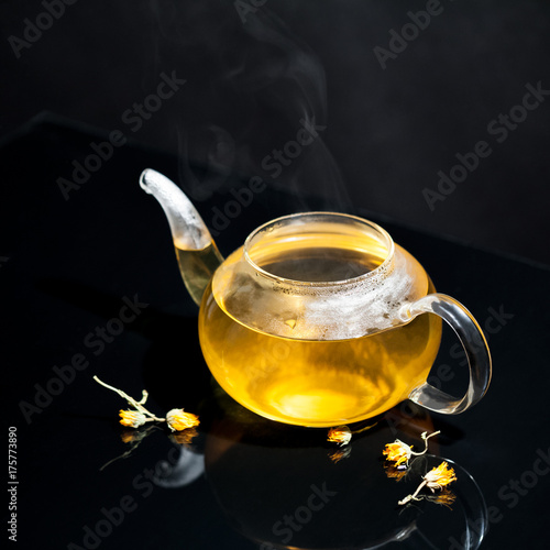 Glass teapot with tea and steam on dark background 