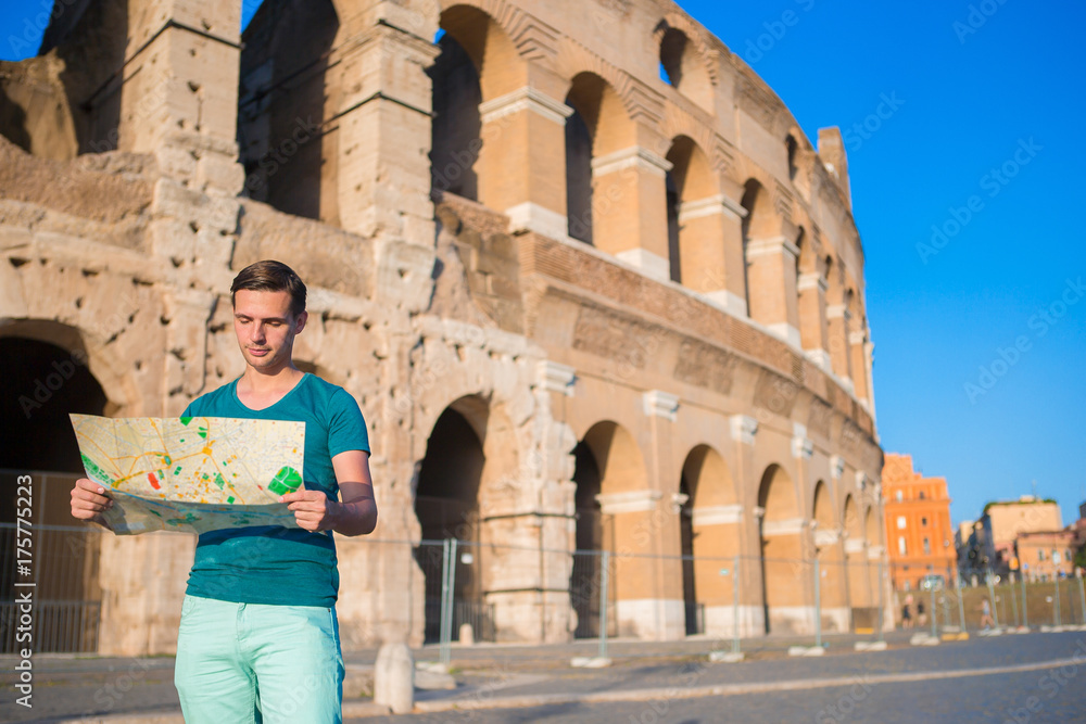Happy guy with map in front of Colosseum. Young man searching the attraction background the famous area in Rome, Italy