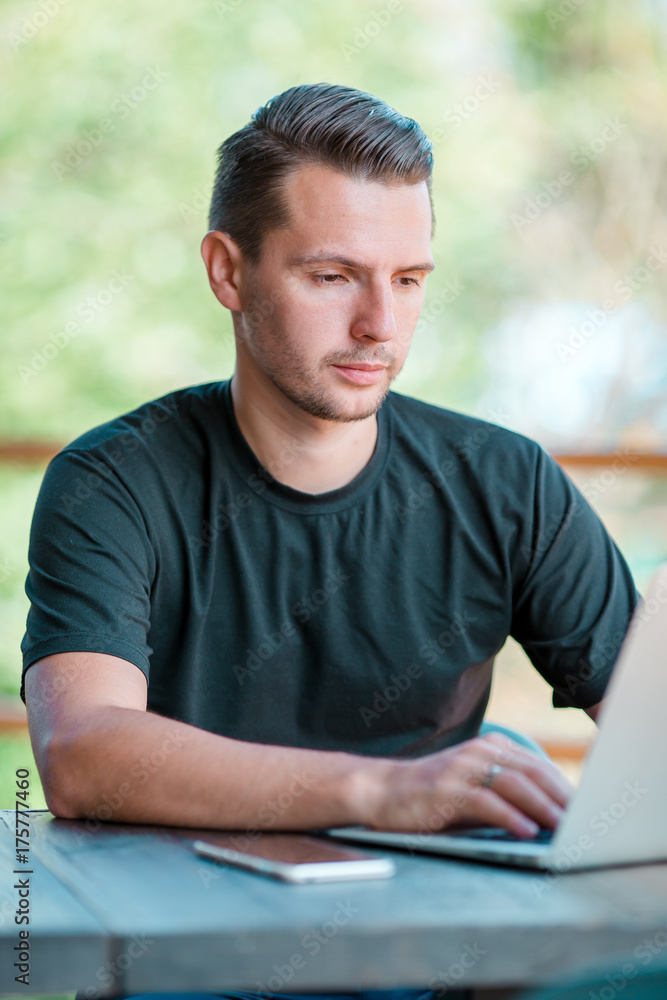Young man with laptop in outdoor cafe drinking coffee. Man using mobile smartphone.