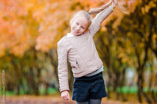 Happy adorable little girl having fun outdoors at beautiful autumn day