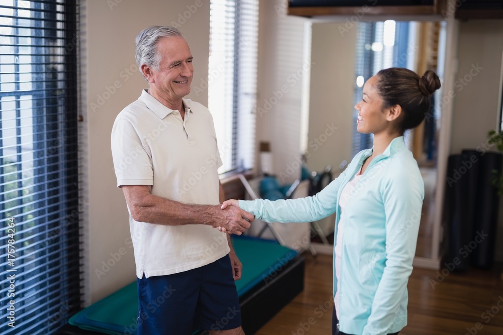 Smiling senior male patient shaking hands with female therapist Smiling senior male patient shaking hands with female therapist