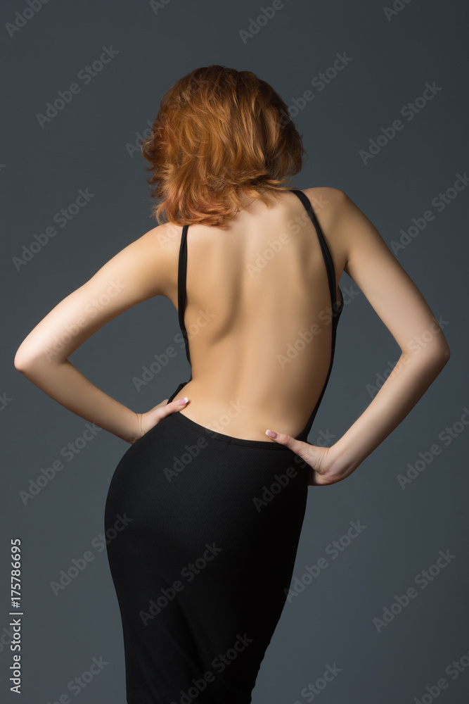 Fototapeta premium beautiful red-haired girl in a black dress on a gray background 