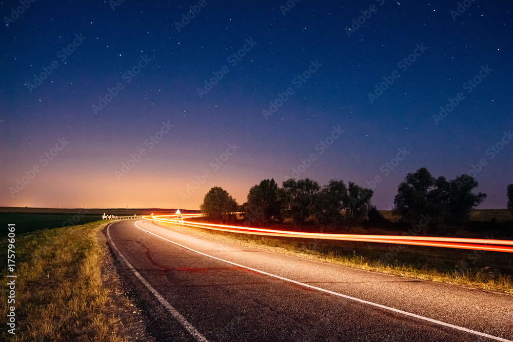 Traces from car headlights in a night landscape with a road under the starry sky
