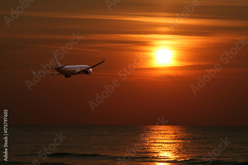 plane flying over the sea towards the setting sun