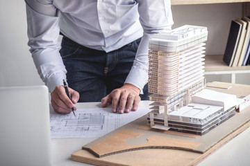 Engineering or Creative architect in construction project, Engineers hands working on construction blueprint and building model at a workplace in office, Building and architecture concept