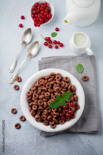 Healthy breakfast with chocolate corn rings, red currant berries, yogurt and tea on a gray concrete background. Selective focus. Top view. Copy space.