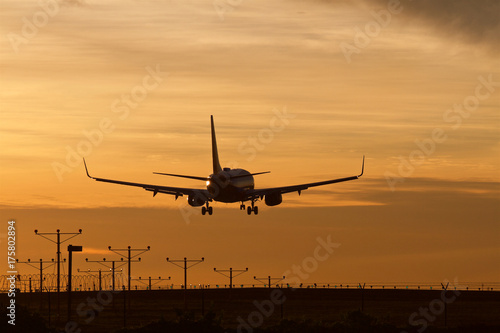 Commercial airliner lands in silhouette during a golden sunset.