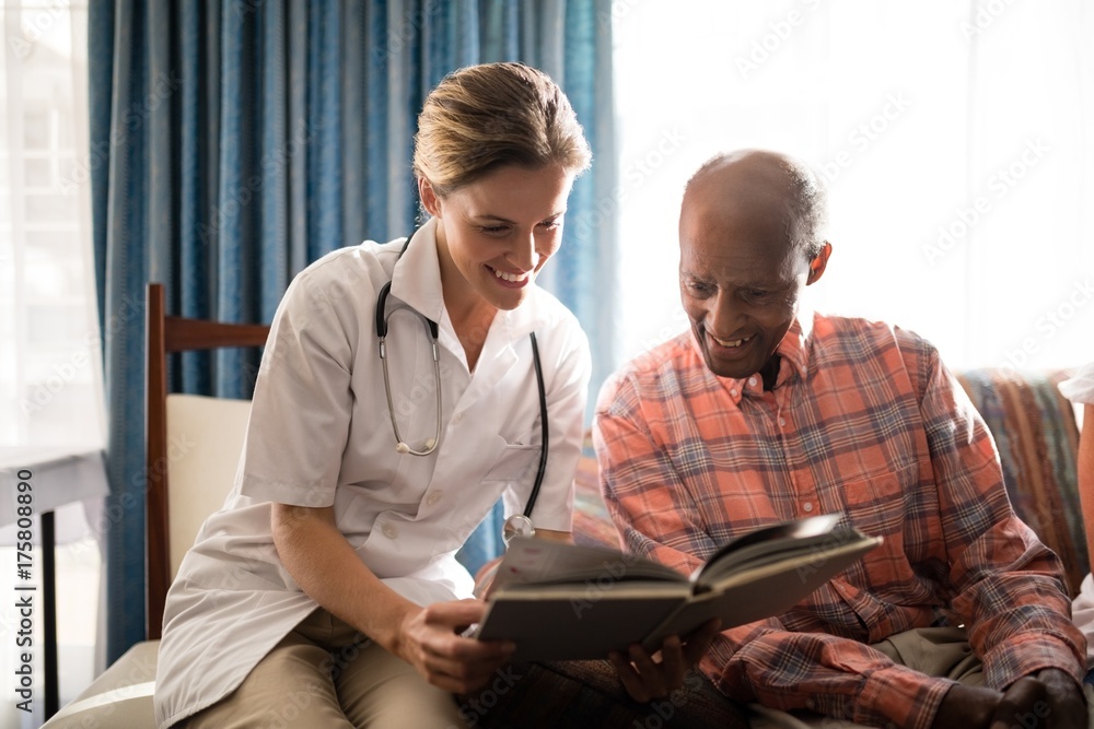 Smiling female doctor reading book with senior man sitting on Smiling female doctor reading book with senior man sitting on