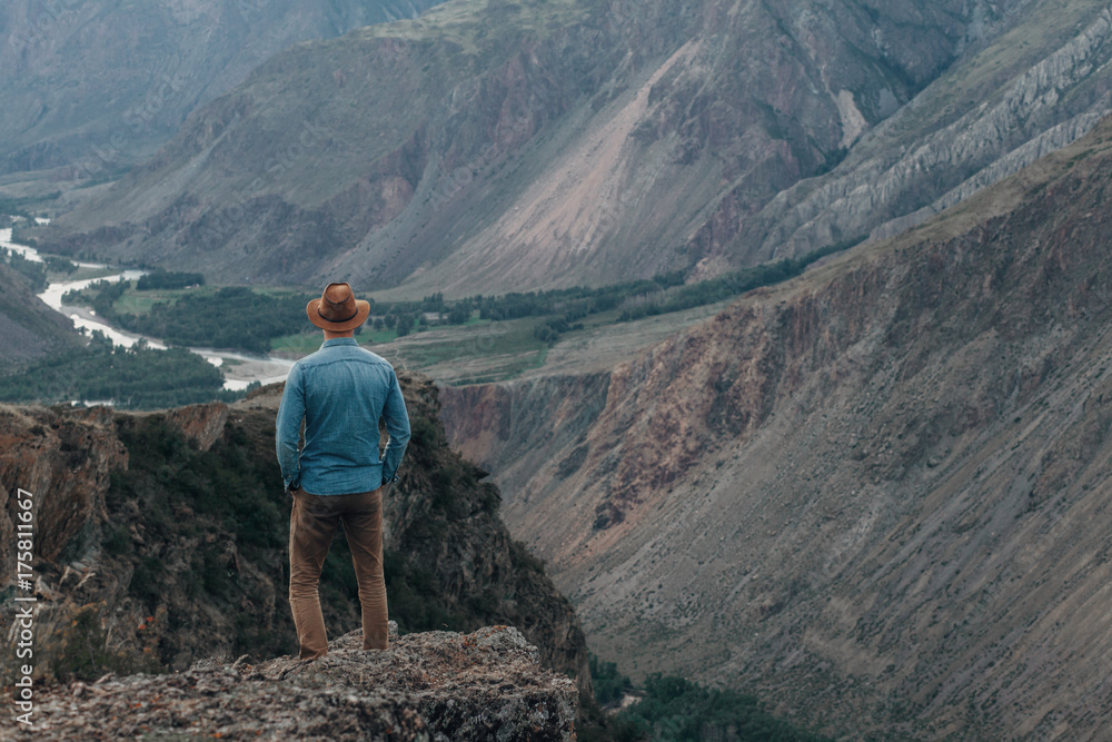 Naklejka premium The traveler in a hat costs on the edge of the high rock and looks to the valley of a canyon