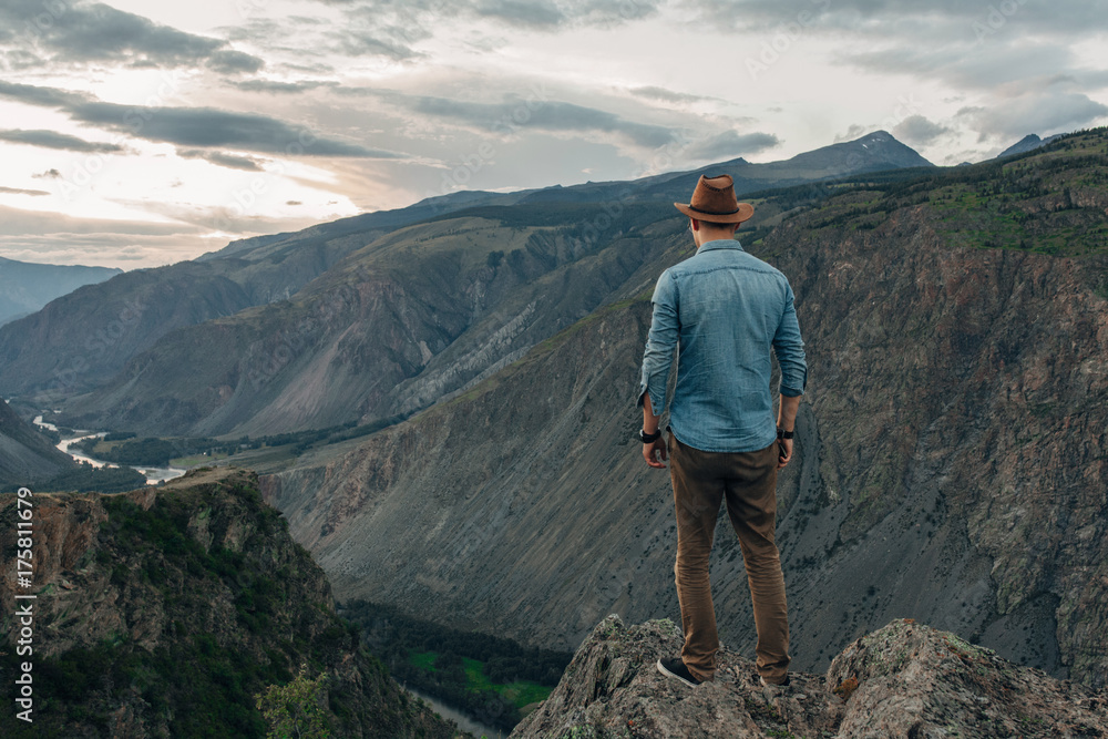 Naklejka premium The traveler in a hat costs on the edge of the high rock and looks to the valley of a canyon