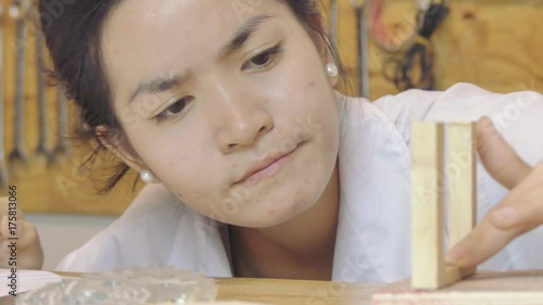 Close up of an Asian  female youth as she tests then glues pieces of a wooden model together in a maker lab / co-working space.  She uses a hot glue gun to seal them together. photo